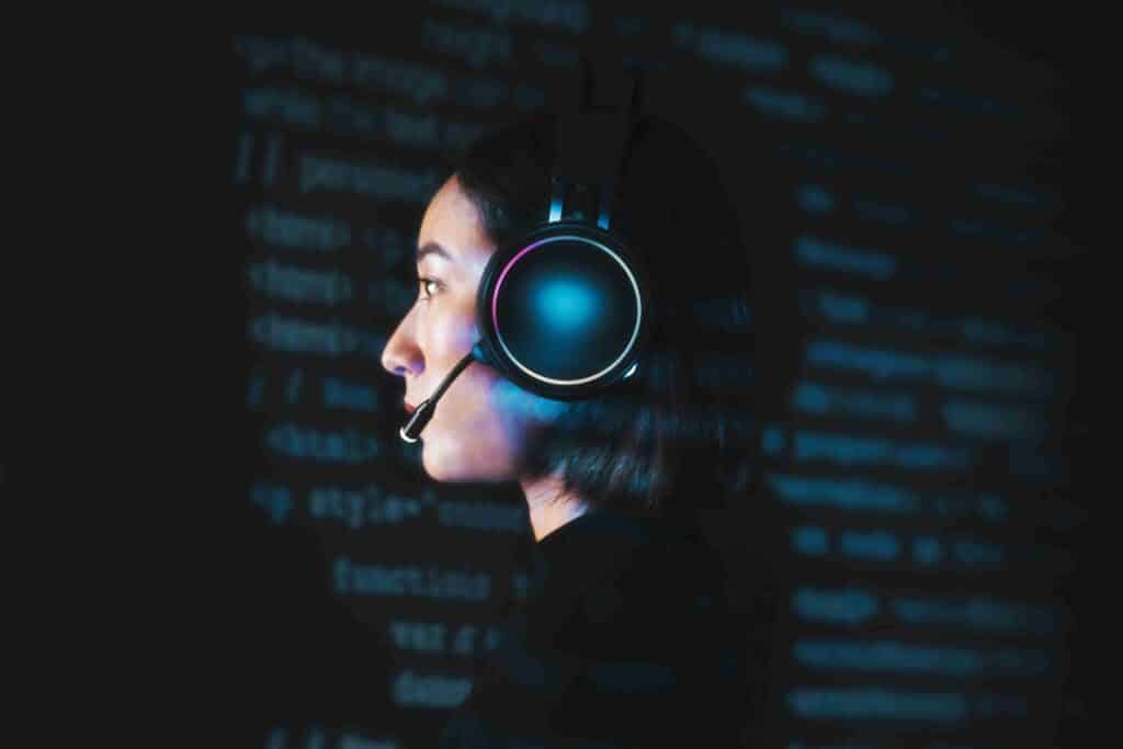 Mulher usando headset diante de tela com códigos, representando interação humano-IA.