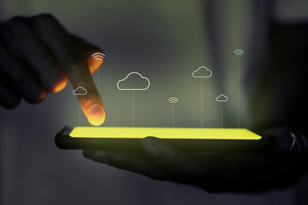Pessoa usando smartphone com ícones de nuvens e sinal de Wi-Fi, simbolizando conexão de cloud computing e tecnologia móvel.