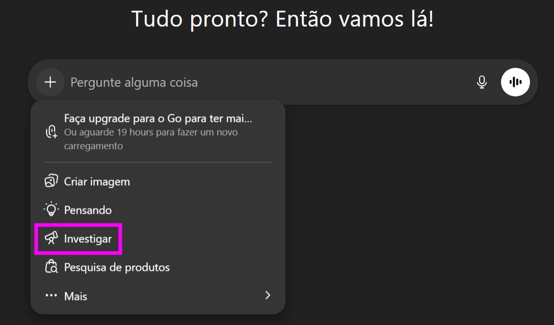 Interface do ChatGPT em modo escuro, com o menu de ações aberto abaixo do campo “Pergunte alguma coisa”. Entre as opções listadas — “Criar imagem”, “Pensando”, “Investigar”, “Pesquisa de produtos” e “Mais” — a opção “Investigar” está destacada com um retângulo rosa. Na parte superior aparece o texto “Tudo pronto? Então vamos lá!”