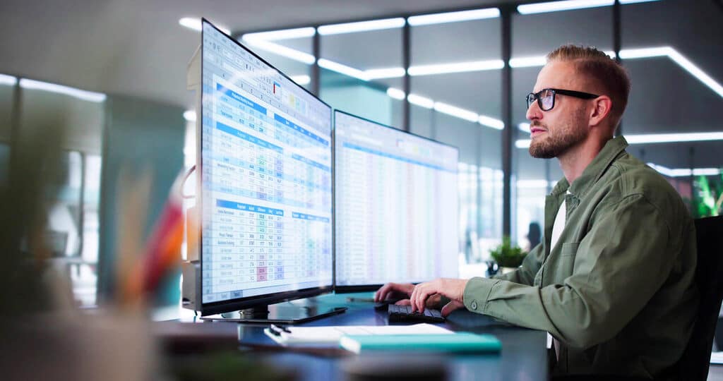 Profissional analisando modelos de planilhas para RH no Excel em ambiente corporativo com múltiplos relatórios.