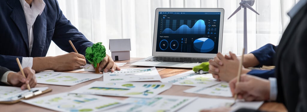 Equipe avaliando relatórios financeiros e dashboard no laptop durante planejamento estratégico com ferramentas de BI.