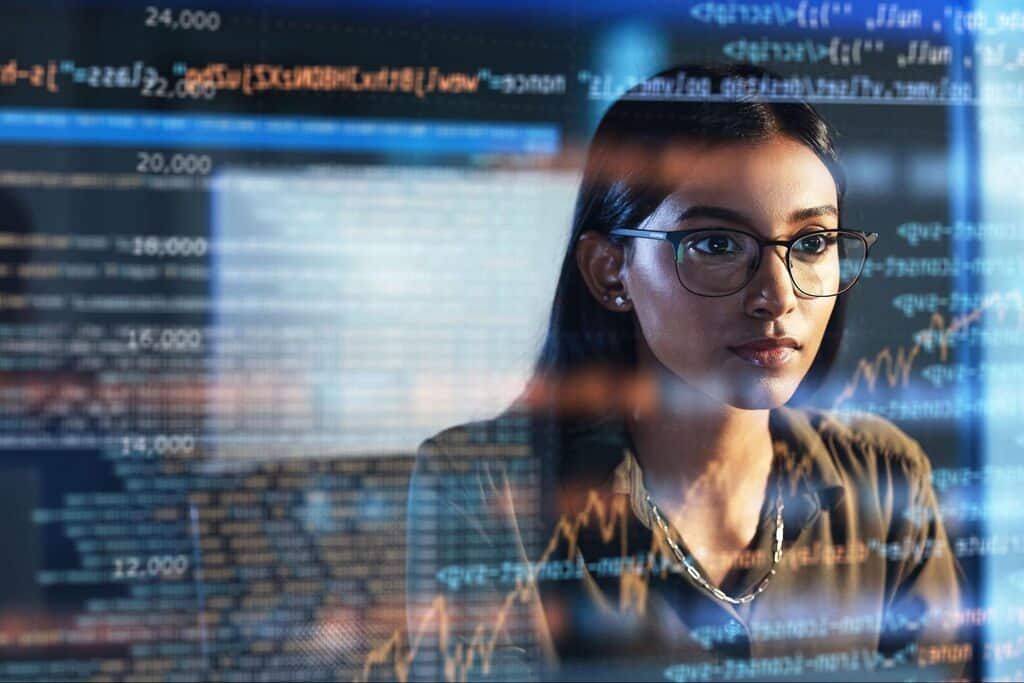 Jovem estudante da área de dados olhando para tela de computador com vários números e códigos.