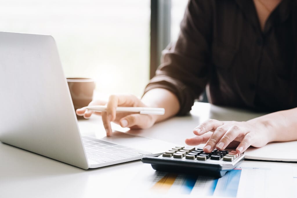 Pessoa utilizando calculadora e notebook realiza projeções financeiras detalhadas aplicando CAGR para Excel diariamente corretamente.